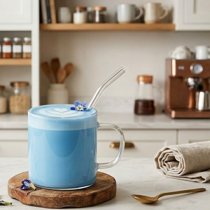 Blue latte in a glass with a straw on a wooden coaster in a kitchen setting.